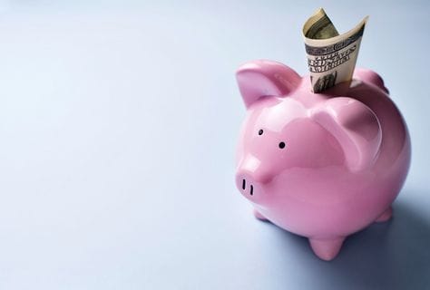 High angle view of a pink ceramic piggy bank with a dollar bill in the slot over a grey background with copyspace